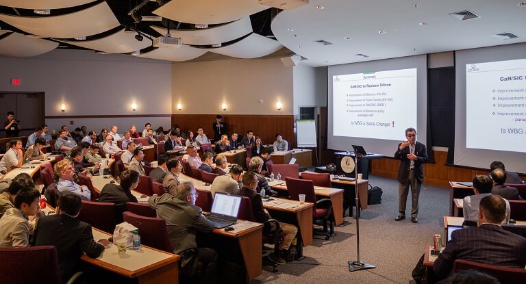 A speaker lectures to a crowded conference room.