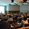 A speaker lectures to a crowded conference room.